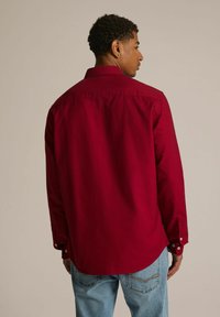 Czerwona, długorękawowa koszula z kołnierzykiem zapinanym na guziki, z teksturowanej bawełny, z białymi guzikami przy mankietach, widok z tyłu.