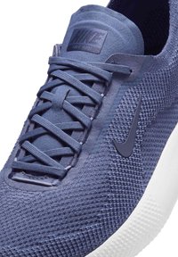 Blå mesh sneakers med en tekstureret overflade, tonale snørebånd, en gummisåler og et mat Nike-logo på siden.