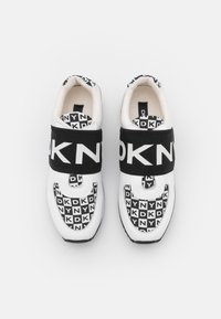 Die Sneakers verfügen über ein schwarzes und weißes Textil-Obermaterial mit einem sich wiederholenden Logo-Muster und einem breiten schwarzen Riemen, der mit "DKNY" beschriftet ist. Abgerundete Zehenform.
