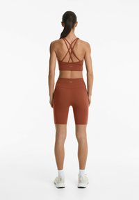Rostfärgad sport-bh med korsade axelremmar, matchad med höga cykelshorts. Slät textur, minimal branding på midjebandet.