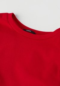 Rotes Baumwoll-T-Shirt mit Rundhalsausschnitt und kurzen Ärmeln. Es hat eine glatte Textur und ein kleines schwarzes Etikett am Hals.