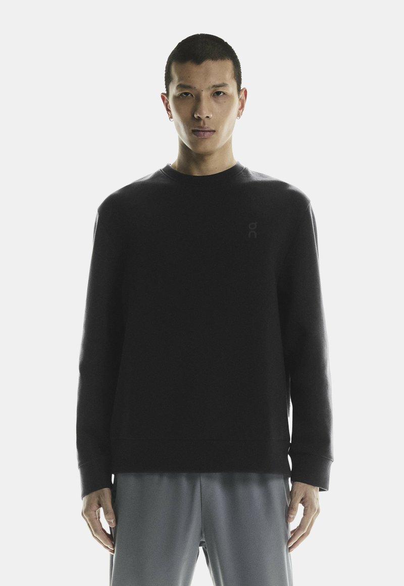 Zwarte sweatshirt met lange mouwen van zachte stof, voorzien van een ronde hals en een subtiele logo op de borst, gecombineerd met lichtgrijze shorts.