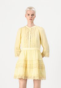 Vestido amarillo con mangas largas abullonadas, botonadura frontal y borde de encaje. Presenta una falda de capas y bordados detallados a lo largo del corpiño y las mangas.