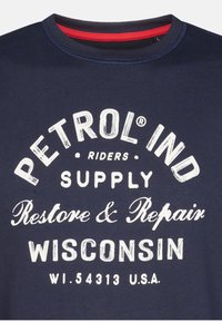 Tmavomodré bavlnené tričko s bielym textom: "PETROL IND SUPPLY Restore & Repair WISCONSIN WI.54313 U.S.A." Červený akcent na výstrihu.