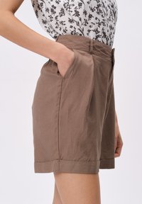Brązowe, dopasowane szorty o strukturalnym kroju, z bocznymi kieszeniami, podwiniętymi nogawkami i lekkim materiałem. Stylizowane z kwiatową bluzką.