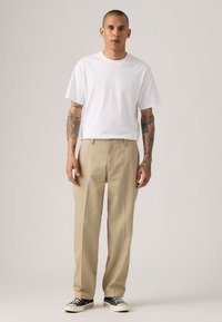 White cotton T-shirt with short sleeves, paired with light beige pleated trousers. Black and white sneakers complete the outfit.