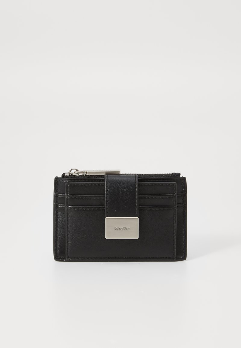 Svart skinnlommebok med glidelås, metalllogo, og kortlommer; glatt tekstur med pent søm.