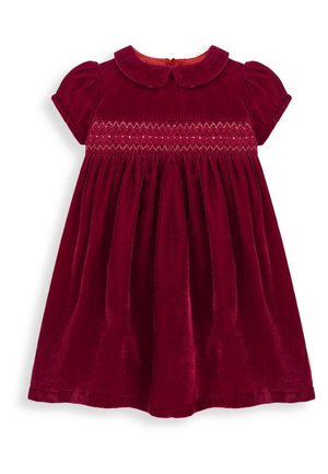 Robe en velours rouge avec un col rond, des manches courtes bouffantes et un corsage smocké avec un détail en zigzag. Jupe évasée avec une texture douce.