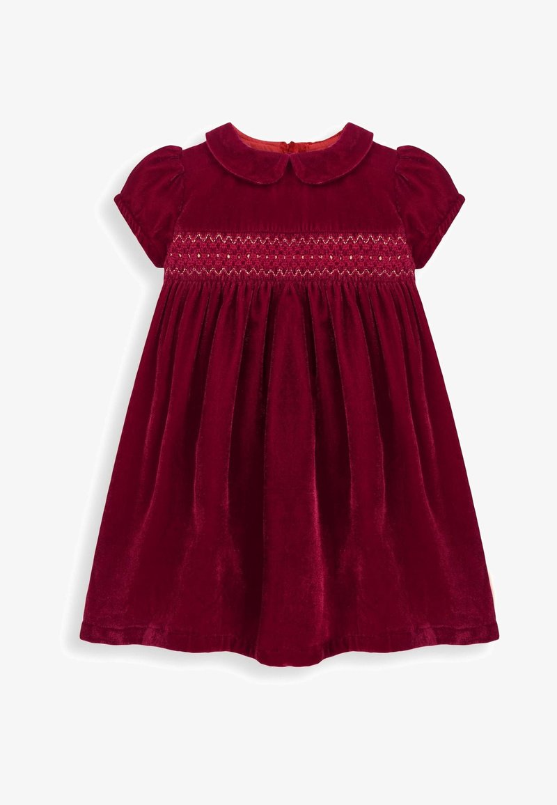 Robe en velours rouge avec un col rond, des manches courtes bouffantes et un corsage smocké avec un détail en zigzag. Jupe évasée avec une texture douce.