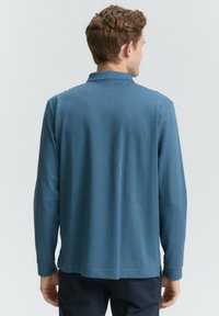 Langærmet polo skjorte i blå, med en klassisk krave og lige kant. Fremstillet af blødt, tekstureret stof med minimal detaljering.