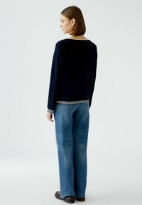 Marineblaue Strickpullover mit kontrastierenden weißen Streifen am Saum und an den Bündchen, kombiniert mit hellblauen, lässigen Weitbeinjeans. Glatte Textur, lockerer Schnitt.