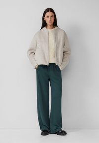 Veste bomber gris clair avec col côtelé et fermeture éclair, associée à un pantalon large vert foncé et des chaussures à plateforme noires.