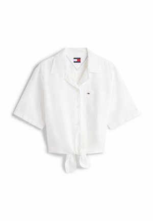 Camisa blanca de manga corta con nudo en la parte delantera, con un cuello con muesca y un solo bolsillo en el pecho. Fabricada en un material ligero.