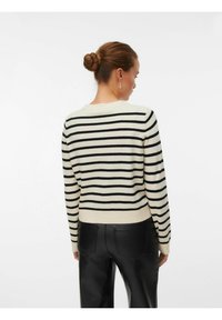 Pull rayé en crème et noir, avec un col rond et des manches longues, doté d'une finition ajustée. Le modèle porte un pantalon noir.