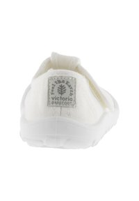 Zapato blanco de tela tipo slip-on con parte superior texturizada, detalle elástico y suela de goma blanca. Presenta una pequeña etiqueta de logo en la parte trasera.