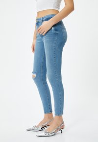 Smala jeans i ljusblå denim med slitning vid knäet, kombinerat med silverfärgade slingback-skor. Slät textur och figurnära design.