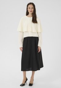 Fehér kötött pulóver réteges köpeny dizájnnal, fekete, áramló midi szoknyával és fekete magassarkú cipővel párosítva. Egyszerű, elegáns stílus.