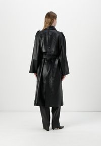 Black leather trench coat with a belted waist, wide sleeves, and a back button detail. Smooth texture, knee-length design.