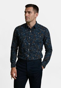 Donkerblauwe shirt met een bladerenpatroon in goud en wit, met knoopsluiting aan de voorkant, lange mouwen en een klassieke kraag, gecombineerd met donkere broek.