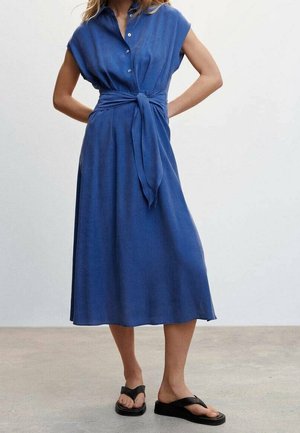 Robe bleu, longueur genou, avec un col de chemise, des manches courtes, des boutons à l'avant et une taille nouée. Tissu lisse, portée avec des sandales noires.