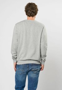 Grijze sweatshirt met lange mouwen, geribbelde manchetten en zoom, gemaakt van zachte stof, gecombineerd met blauwe denim jeans met achterzakken.