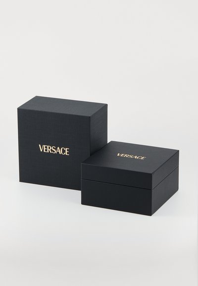Dva čierne textúrované darčekové krabice so zlatým logom "VERSACE", jedna väčšia a menšia vložená krabica, obe štvorcového tvaru.