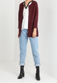 Burgundský texturovaný cardigan, bílý top s výstřihem do V, světle modré rifle s ohrnováním a černé kozačky po kolena se čtveratým podpatkem.