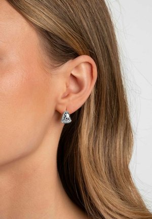 Silberschmuck-Ohrringe mit dreieckiger Form und einer strukturierten Oberfläche, verziert mit dekorativen Nieten, getragen am Ohrläppchen.