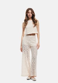 Conjunto de dos piezas de crochet en marfil, que incluye un top sin mangas y corto, y pantalones de pierna amplia con patrones circulares intrincados y una textura transparente.