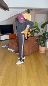 Καφέ φόρμες με άσπρες ρίγες στο πλάι, σε συνδυασμό με ένα σκούρο μπλουζάκι με μακριά μανίκια και άσπρα αθλητικά παπούτσια, σε μια ζεστή εσωτερική ατμόσφαιρα.