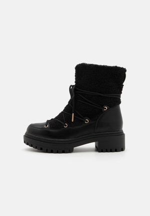 Botas negras hasta el tobillo con un upper texturizado de material similar a la lana y cuero suave, con detalles en tono dorado y una suela de goma gruesa.