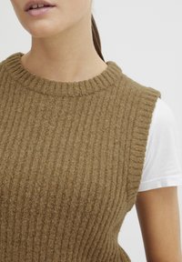Brun ribbestrikket vest med rund halslinning og ermeløs design, lagd over en hvit T-skjorte med korte ermer. Myk tekstur med subtile detaljer.