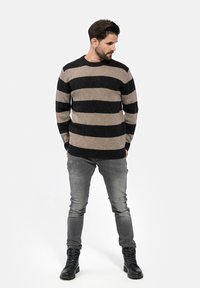Schwarz-beige gestreifter Pullover aus strukturiertem Strick, mit Rundhalsausschnitt. Getragen mit verwaschenen grauen Jeans und schwarzen Schnürstiefeln.