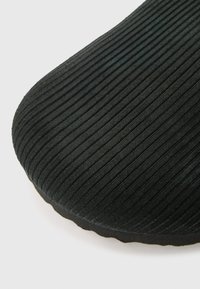 Juodas guminiu padu su vertikaliomis briaunomis ir reljefine paviršiaus tekstūra. Apvalinti kraštai ir šiek tiek išlenkta forma.