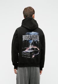 Melna kapuce ar grafisku dizainu, kurā attēlots auto un pilsētas ainava. Ar kapuci, brīvs piegriezums, ar ribotām aprocēm un apakšmalu.