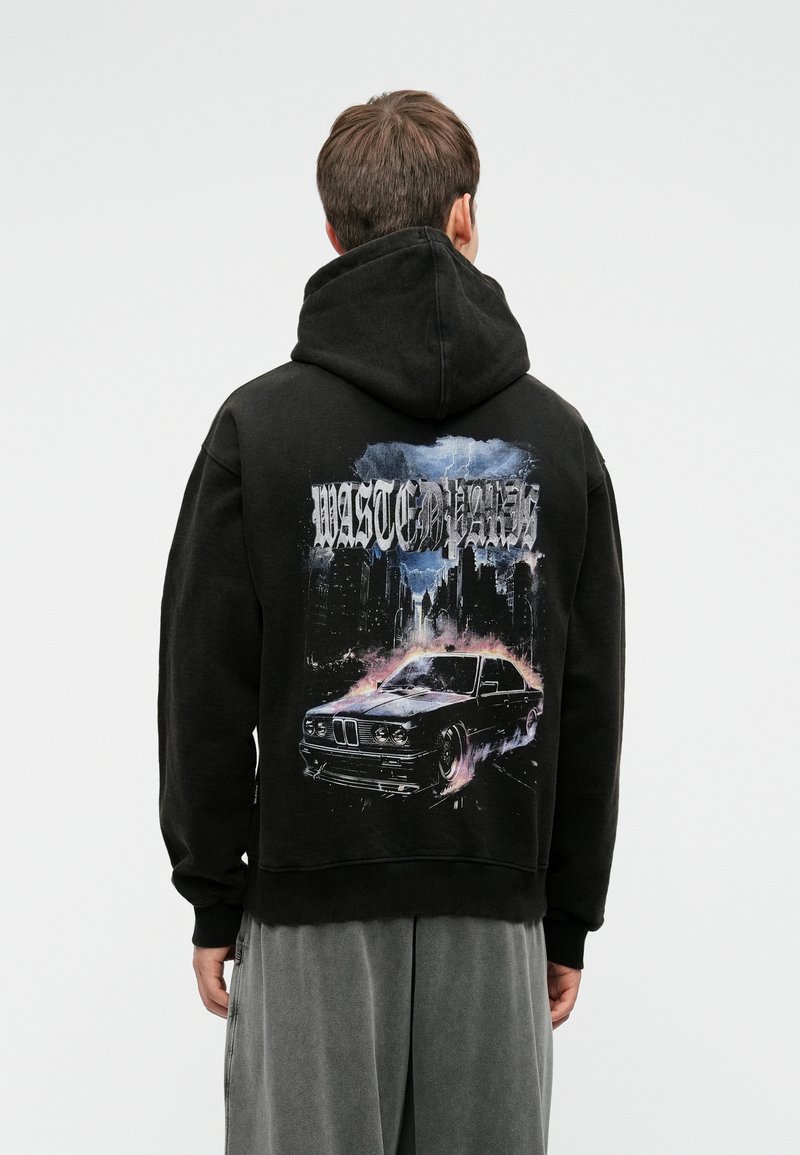 Melna kapuce ar grafisku dizainu, kurā attēlots auto un pilsētas ainava. Ar kapuci, brīvs piegriezums, ar ribotām aprocēm un apakšmalu.