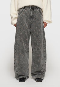 Jeans de pierna ancha en denim gris deslavado, con un sutil patrón floral en marrón claro, de talle alto y con detalles de dobladillo desgastado.