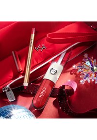 Producto labial KIKO Milano en un tubo transparente y rojo, un lápiz labial dorado, lápiz labial rojo y un adorno de copo de nieve brillante sobre una superficie roja.