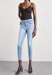 Top de tirantes negro con texturizado, combinado con jeans de mezclilla azul claro. Los jeans son ajustados, con un largo recortado y dobladillo deshilachado, complementados con zapatillas de tacón negro.
