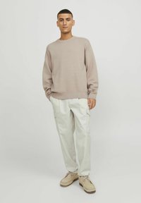 Maglione beige a maglia abbinato a pantaloni cargo crema chiaro. Footwear in camoscio tan, con punta tonda e chiusura con lacci. Stile semplice e minimalista.