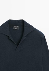 Granatowy wełniany sweter typu pulower z prążkowanym kołnierzem i dekoltem w serek. Etykiety wskazują na 100% wełniany materiał, markę i instrukcje pielęgnacji.