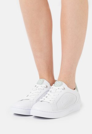 Beine, die weiße Bugatti Low-Top-Sneaker mit Schnürsenkeln tragen, mit hellgrauen Akzenten auf Zunge und Ferse vor weißem Hintergrund.