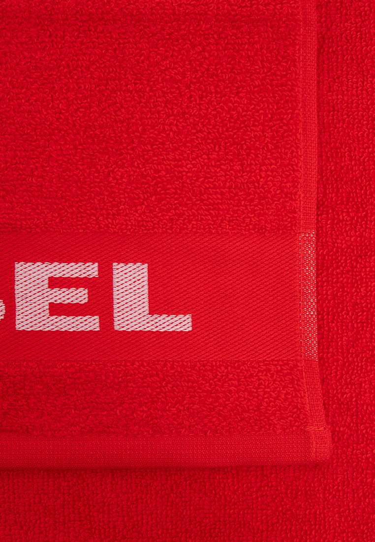 Toalla roja con una superficie texturizada y una banda suave con texto blanco. Los bordes están cuidadosamente acabados, lo que mejora su durabilidad.