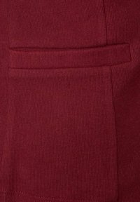 Burgundská bavlněná tkanina s žebrovanou texturou, obsahující našitý boční kapsový detail a hladké okraje, vytvářející upravený vzhled.