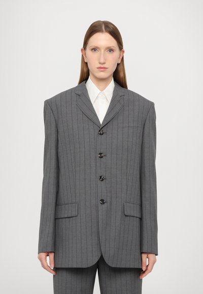 Grå stribede oversized blazer med seks knapper, klapkraver og to forlommer, båret over en hvid skjorte med krave.