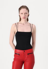 Black spaghetti-strap top with a square neckline, paired with textured red leather pants featuring zippered accents.