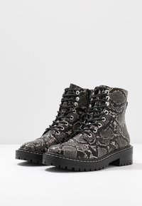 Bottes à lacets noires et grises à motif, avec un design texturé d'aspect peau de serpent, dotées d'oeillets en métal et d'une semelle noire épaisse.
