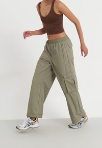 Spodnie cargo w jasnym oliwkowym kolorze, wykonane z lekkiego materiału. Charakteryzują się luźnym krojem, elastycznym paskiem w talii oraz bocznymi kieszeniami. W zestawie z srebrnymi butami do biegania.