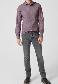 Vinröd skjorta med knapp-up och en liten ficka, kombinerad med grå jeans. Skjortan har ett subtilt mönster och långa ärmar. Svarta skor fulländar outfiten.