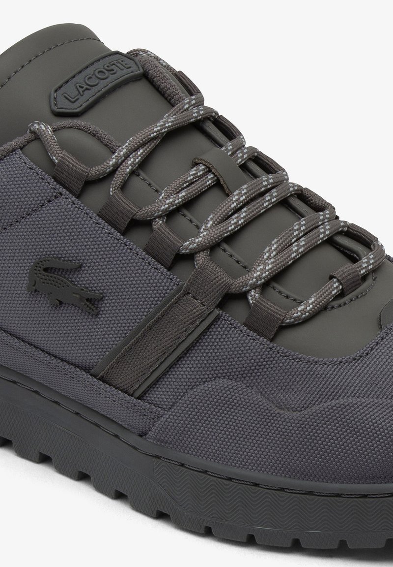 Basket Lacoste gris foncé en tissu texturé, semelle épaisse, écusson de marque et lacets ronds à motif noués à travers des boucles en tissu.